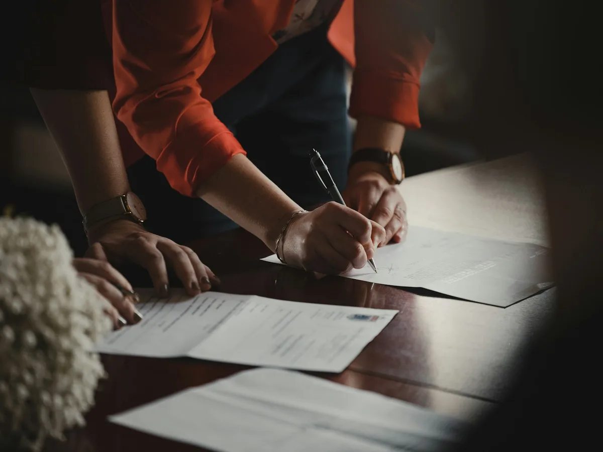 Person signing a home loan contract with a pen on a wooden desk