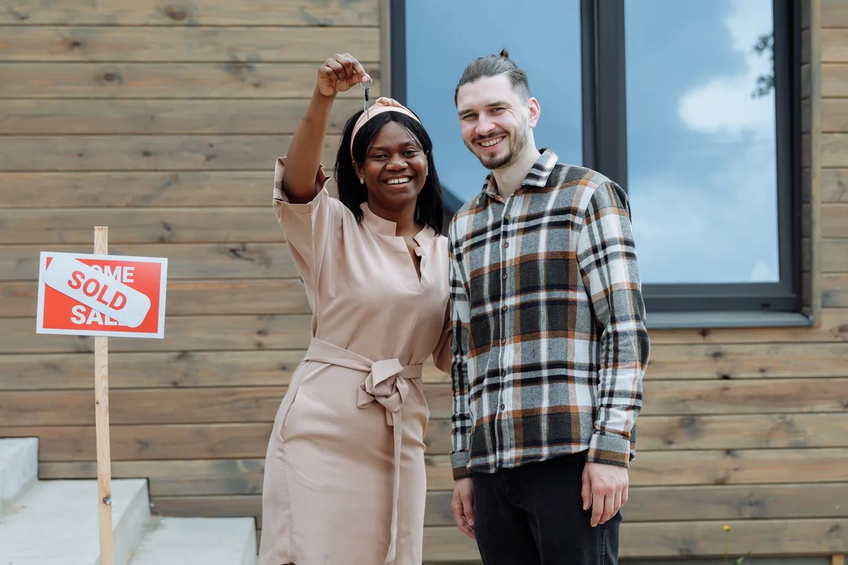 Young couple standing in front of their new home holding keys
