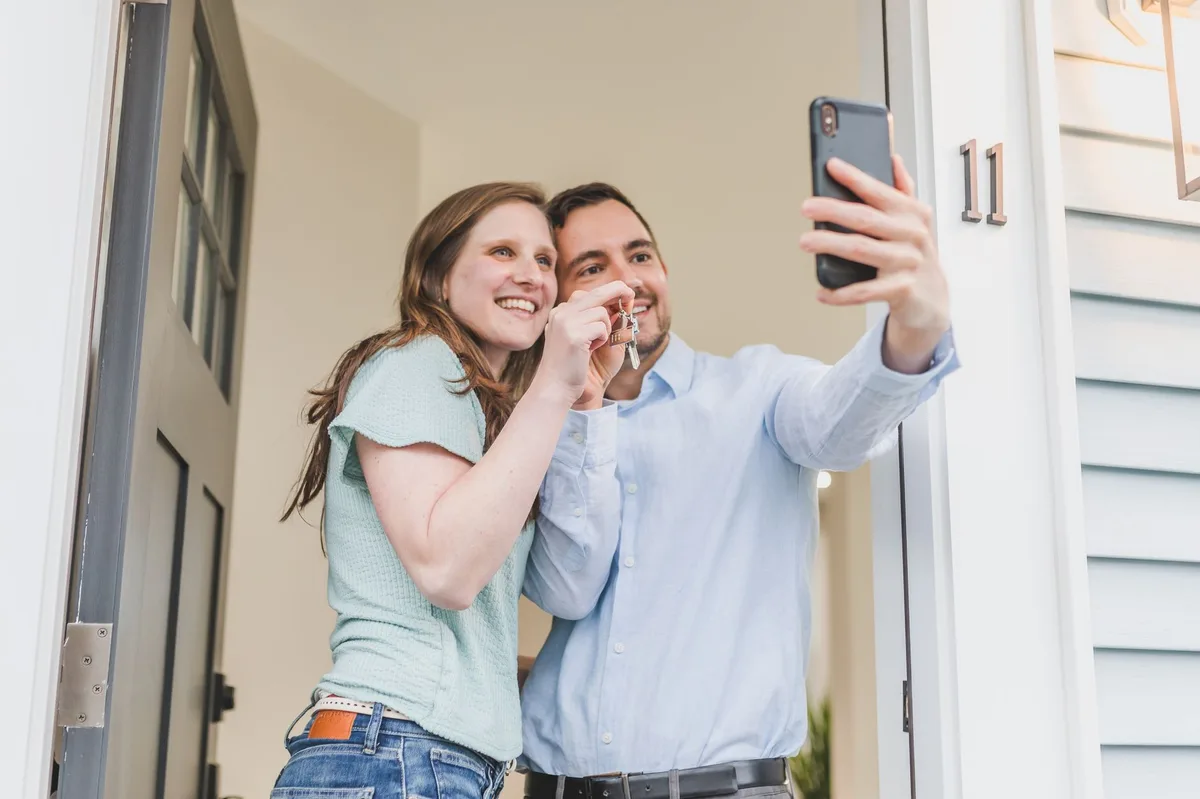 A young couple holding keys in front of their new first home in Canada