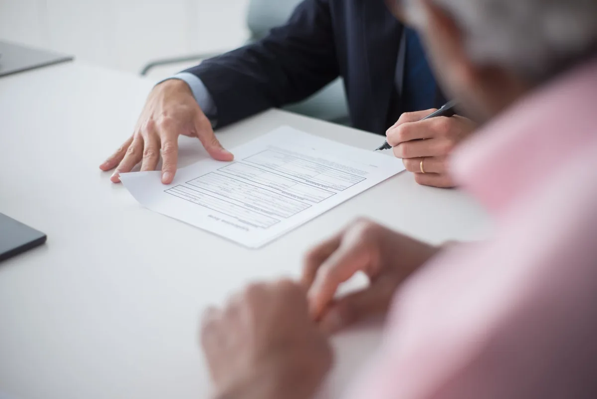 Person signing a contract on a desk with documents