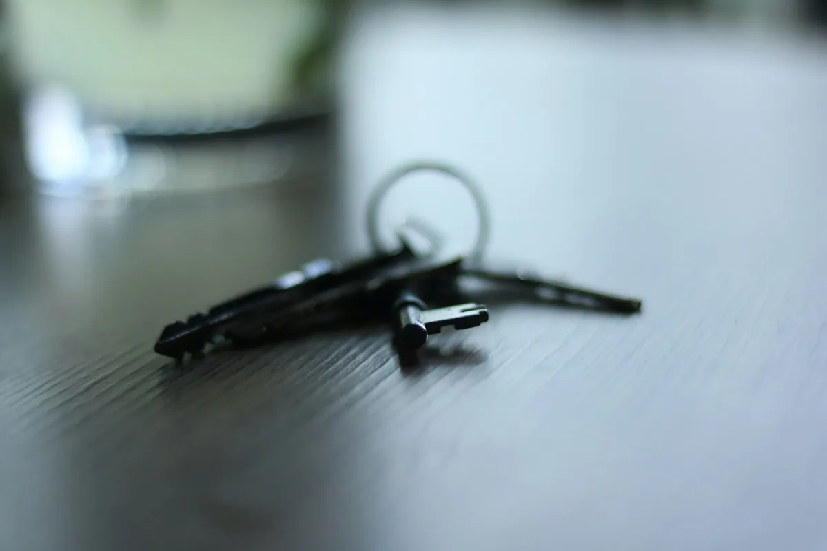 A homeowner signing mortgage documents on a wooden desk next to house keys.