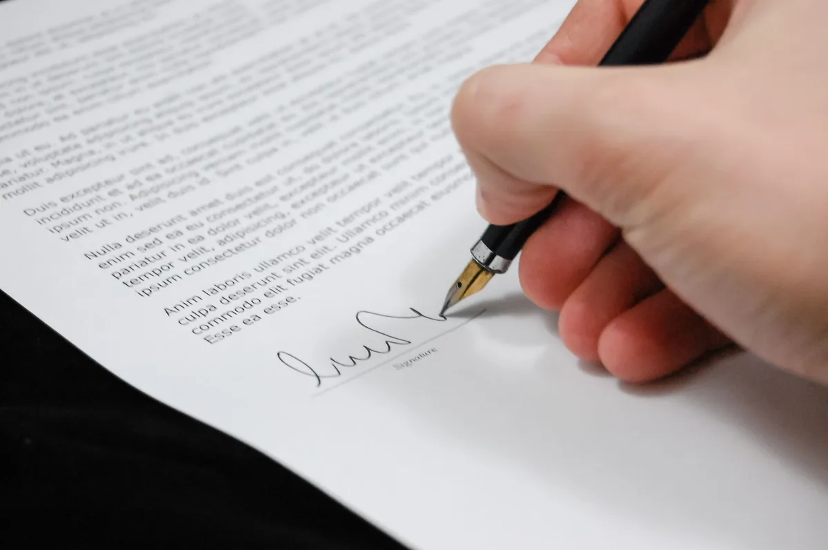 A person signing a contract document with a pen on a desk